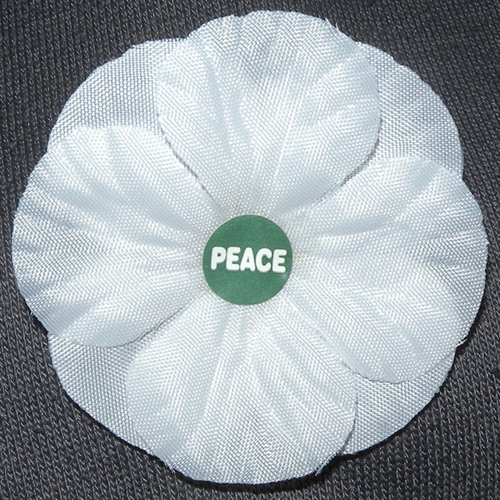 A white fabric poppy with a green centre that reads 'peace'